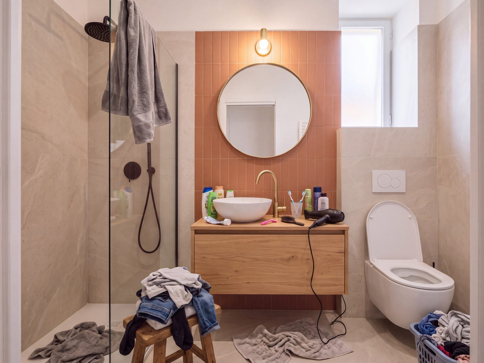 Bagno in disordine: flaconi sul lavabo, asciugamani usati e tavoletta alzata